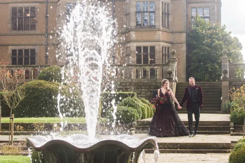 A couple outside a gothic hall with a fountain in front