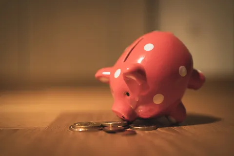 A piggy bank on a table with it's nose tilted towards some coins