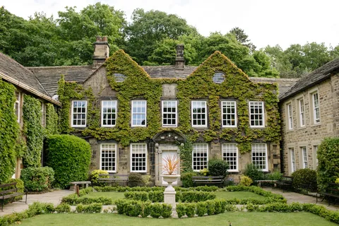 Manor house covered in greenery with a garden in front with benches and shrubbery