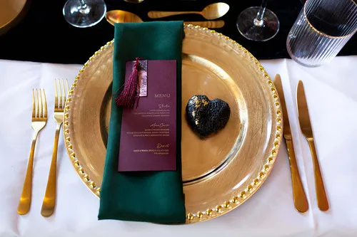 A table setup with gold cuterly with the menu on top of a black napkin